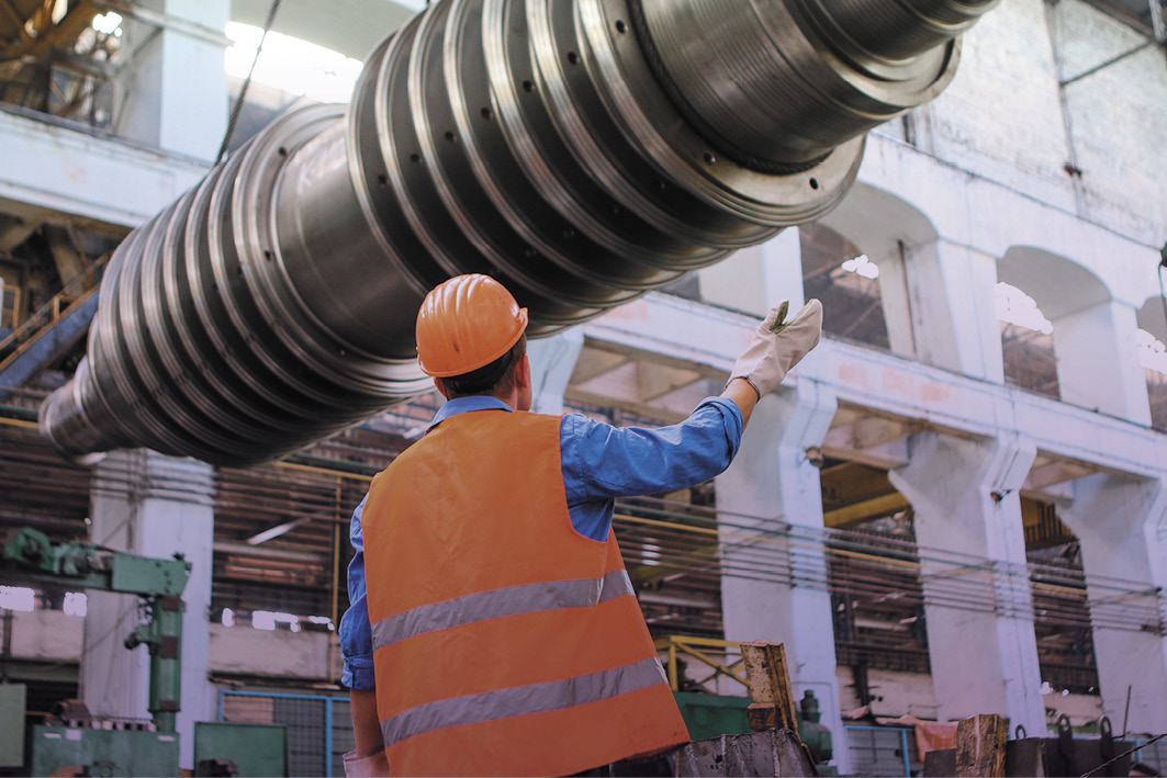 Construction worker guiding a large piece of equipment  in to position by crane driver