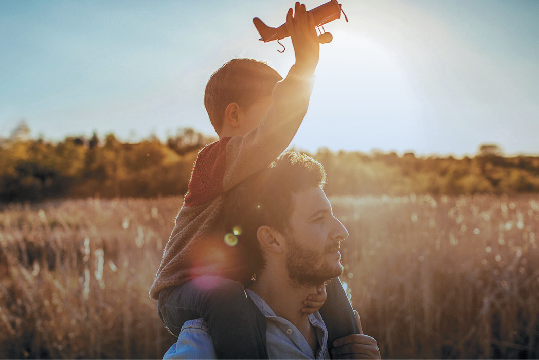 Boy on his father's shoulders holding an aeroplane toy
