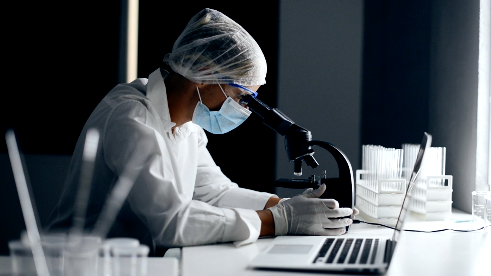 Man looking through microscope, wearing protective equipment