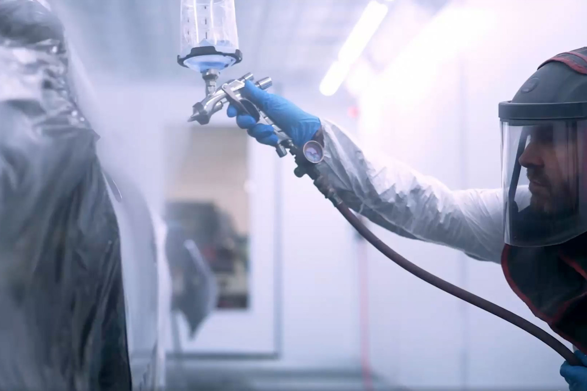 Man in car spray room, dressed in protective equipment, spraying a car