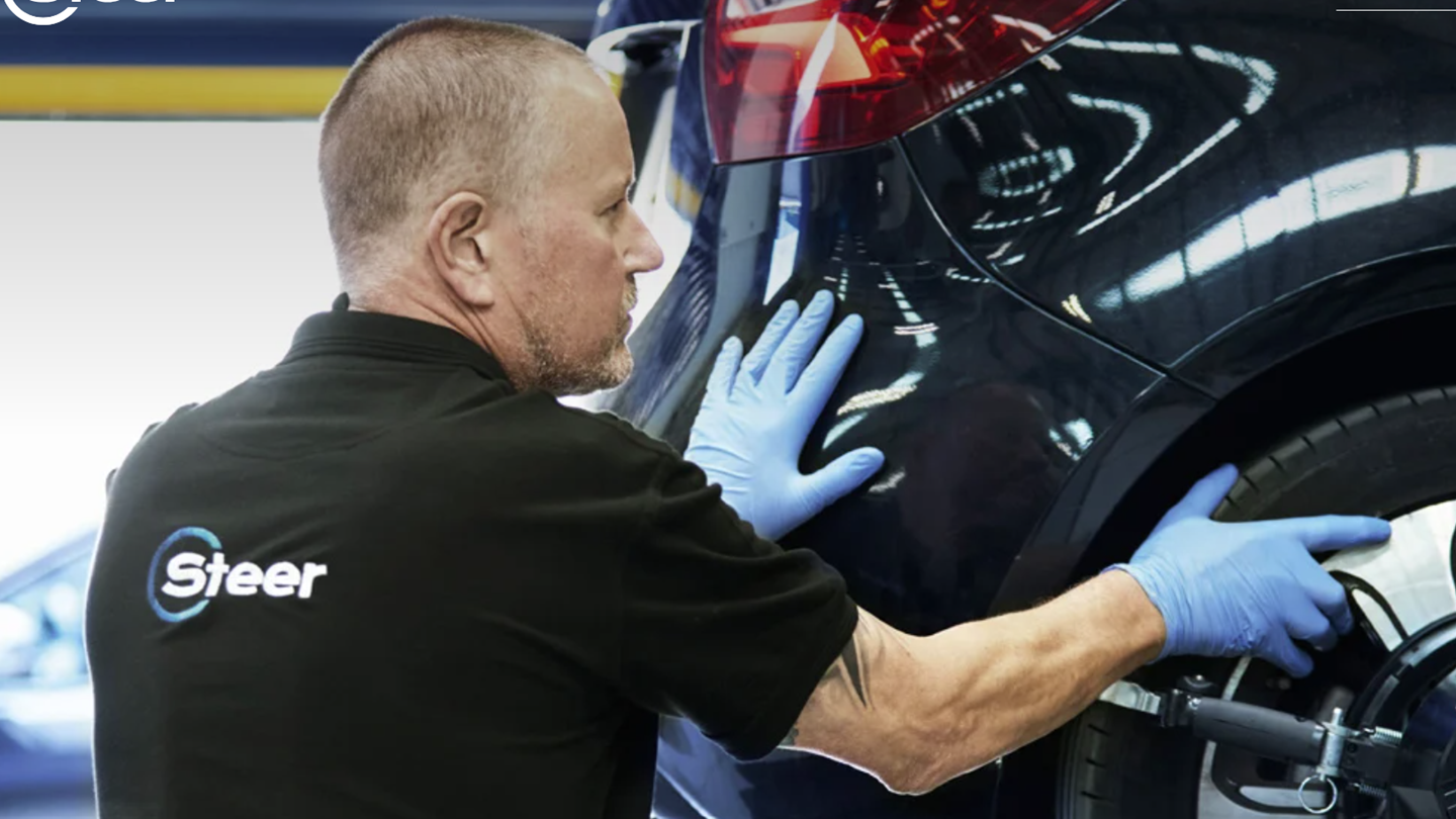 Man fixing a car, wearing a t-shirt with steer automotive logo on its back