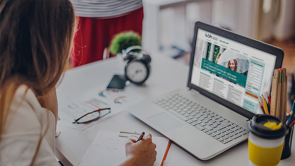 Woman writing at desk, while researching at computer screen